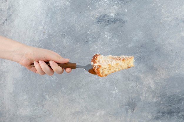 Feminino mão segurando torta doce no fundo de mármore.