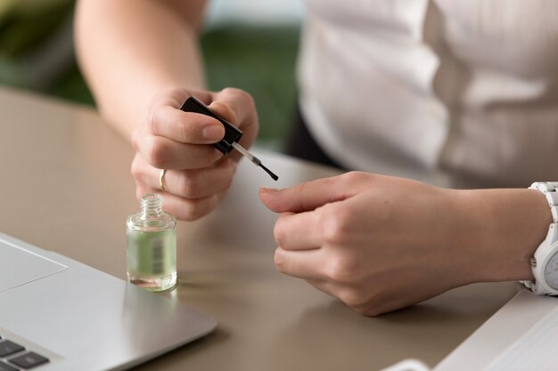 Feminino mãos fazendo manicure no escritório, pintando as unhas, close-up