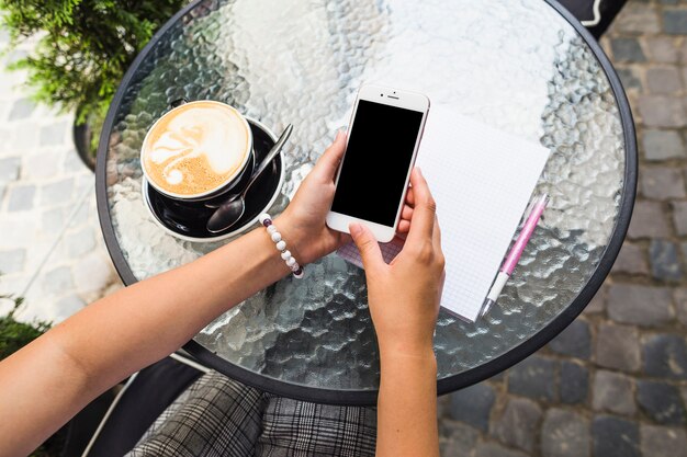 Feminino usando celular com xícara de café sobre a mesa de vidro