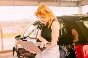 Foto grátis feminino viajante com laptop em pé ao lado do carro