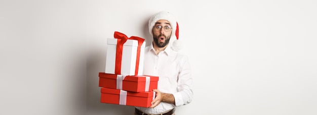 Feriados de inverno e celebração animado homem segurando presentes de natal e parecendo surpreso vestindo sa