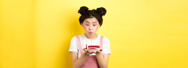 Feriados e celebrações menina asiática boba com maquiagem glamorosa fazendo desejo e soprando vela no nascimento