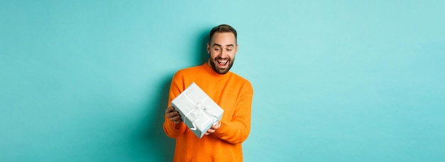 Foto grátis feriados e conceito de celebração animado homem recebendo presente parecendo feliz no presente e sorrindo sta