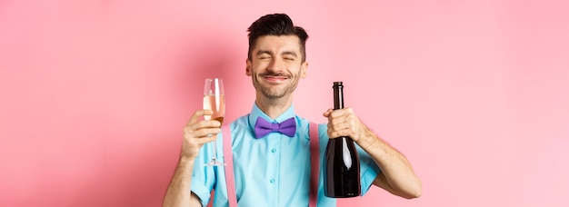 Foto grátis feriados e conceito de celebração homem feliz sorrindo e gostando de beber na festa segurando garrafa de