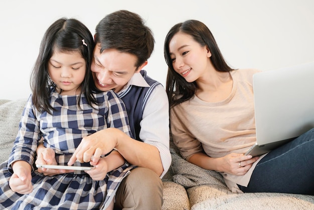 Férias de fim de semana da família asiática da felicidade com a mãe, pai, filha, ficam juntas, usam tablet e laptop em casa fundo interior