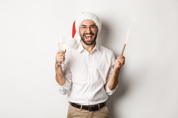 Férias de inverno e celebração. Homem barbudo bonito na festa de ano novo, segurando fogo de artifício e champanhe, usando chapéu de Papai Noel