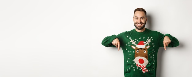 Foto grátis férias de inverno e natal bonito homem sorridente com barba apontando os dedos para baixo e mostrando o baile