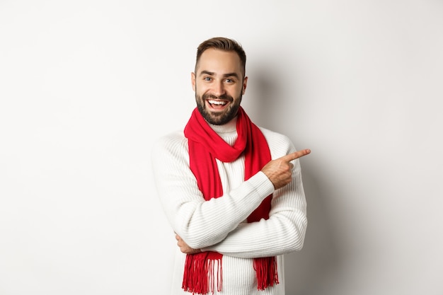 Férias de Natal e conceito de celebração. Homem barbudo feliz apontando o dedo para o espaço da cópia, mostrando a oferta de anúncio, em pé sobre um fundo branco