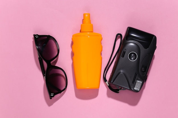 Férias na praia, conceito de viagens. frasco de protetor solar, óculos escuros e câmera em rosa brilhante ensolarado
