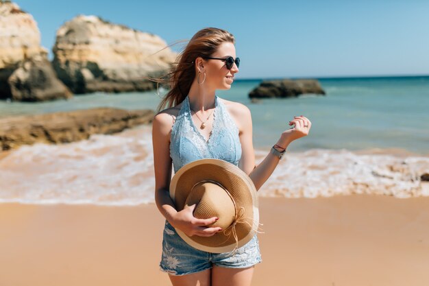 Férias na praia. Linda mulher de chapéu de sol, aproveitando o dia de sol perfeito, caminhando na praia. Felicidade e bem-aventurança.