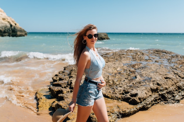 Férias na praia. Linda mulher de chapéu de sol, aproveitando o dia de sol perfeito, caminhando na praia. Felicidade e bem-aventurança.