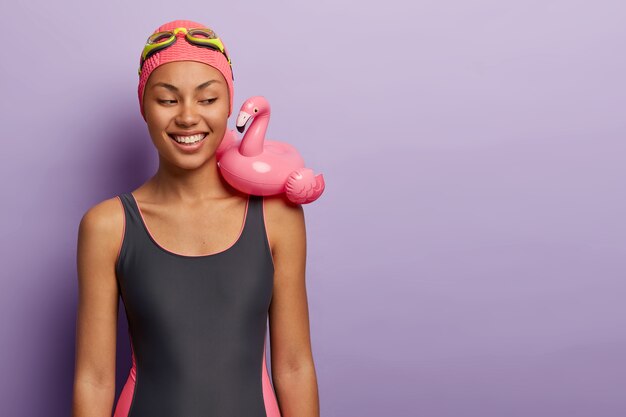 Férias, praia, conceito de verão. Mulher sorridente de pele escura se prepara para a festa na piscina, usa maiô preto e óculos de proteção