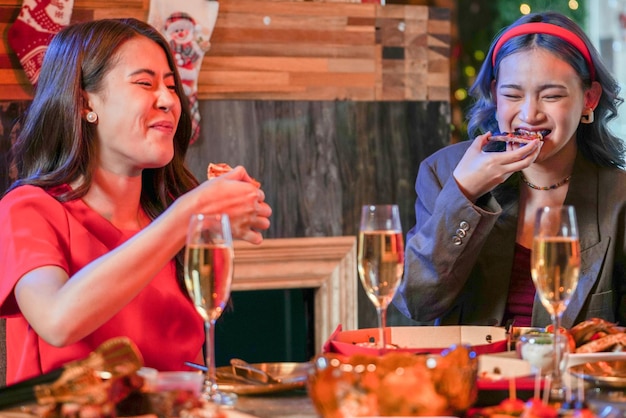 Festa da linda amiga asiática feminina comemorando. mulheres comendo pizza na mesa com lanche e bebida. felicidade amigos celebração da véspera de natal jantar festa comida e champanhe.