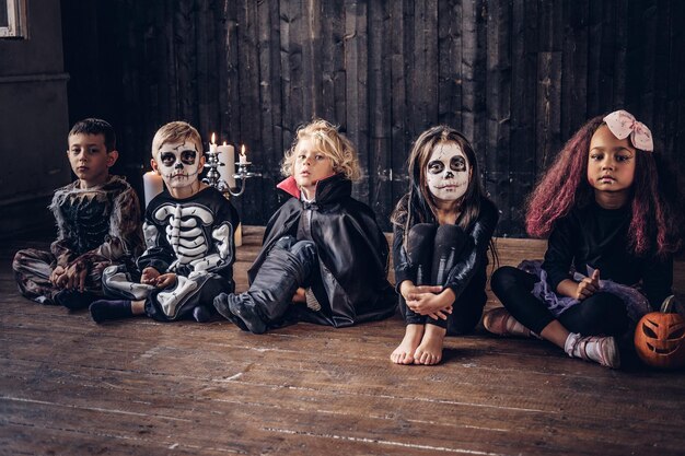 Festa de Halloween com crianças do grupo que se sentam juntas em um piso de madeira em uma casa velha.