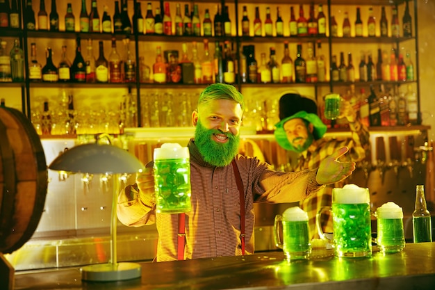 Festa do Dia de São Patrício. Amigos felizes está comemorando e bebendo cerveja verde. Homens e mulheres jovens usando chapéus verdes. Pub Interior.