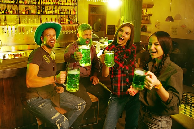 Festa do Dia de São Patrício. Amigos felizes está comemorando e bebendo cerveja verde. Homens e mulheres jovens usando chapéus verdes. Pub Interior.