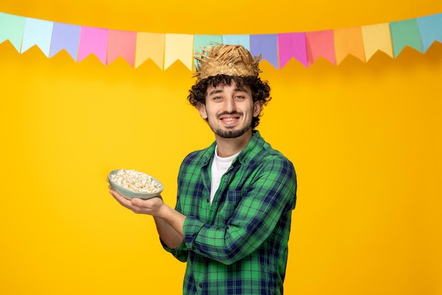 Festa junina jovem bonitinho de chapéu de palha e bandeiras coloridas festival brasileiro segurando pipoca de tigela