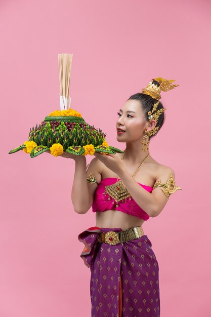 Festival Loy Krathong; mulher com roupa tradicional tailandesa segurando um flutuador decorado
