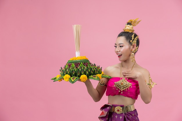 Festival loy krathong; mulher com roupa tradicional tailandesa segurando um flutuador decorado