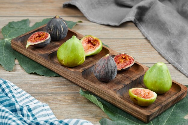 Figos verdes e pretos em uma travessa de madeira com folhas e toalha de mesa. Foto de alta qualidade