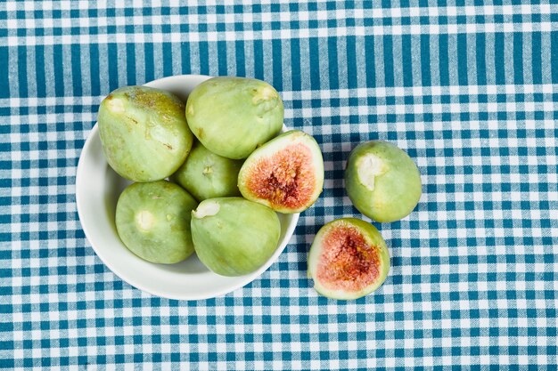 Figos verdes em uma tigela branca e sobre uma mesa de madeira com toalha de mesa azul