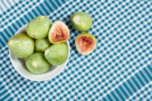 Figos verdes em uma tigela branca e sobre uma toalha de mesa azul