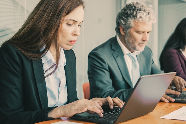 Fila de colegas concentrados sentados em uma mesa e usando computadores.