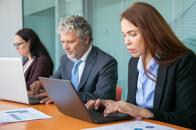 Fila de colegas focados sentados em uma mesa e usando computadores