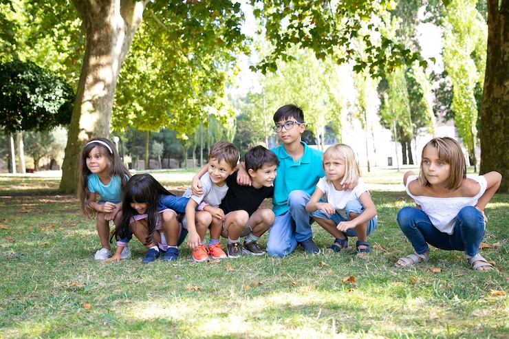Foto grátis fila de crianças felizes fazendo agachamentos no parque, se abraçando, desviando o olhar de empolgação. festa infantil ou conceito de entretenimento