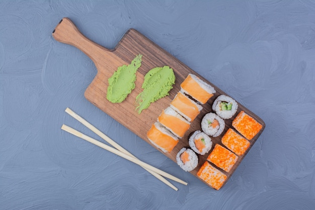 Filadélfia, salmão e saquê maki rolos com wasabi em uma travessa de madeira.