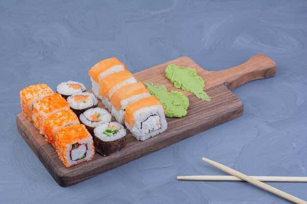 Filadélfia, salmão e saquê maki rolos com wasabi em uma travessa de madeira.