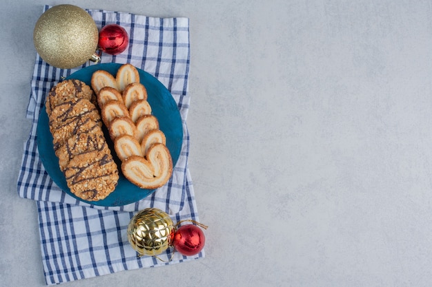 Fileiras de biscoitos em um quadro azul ao lado de enfeites de natal em uma toalha na superfície de mármore