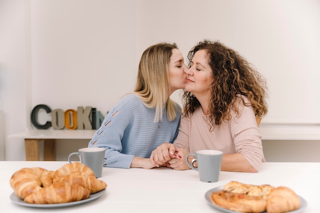 Filha beijando a mãe na bochecha durante café da manhã