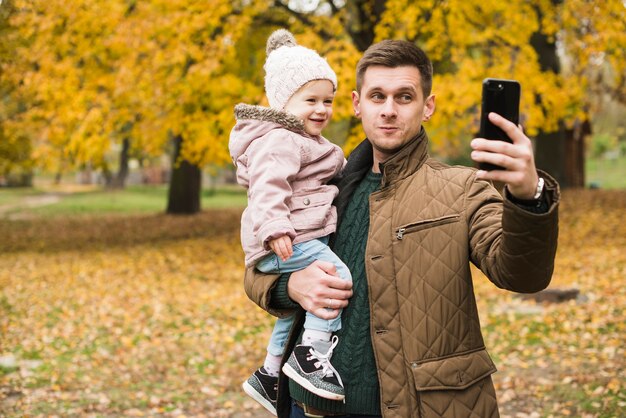 Filha de pai e da criança fazendo selfie no parque outono