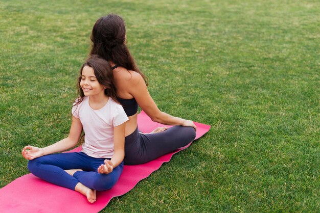 Filha e mãe meditando na grama verde