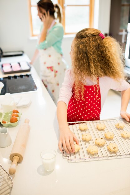 Filha olhando para a mãe, enquanto toma bolinhos na cozinha