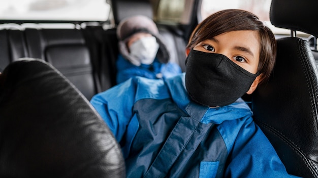 Filhos de tiro médio usando máscaras no carro