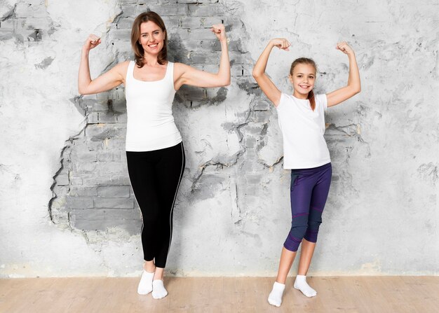 Filmagem completa mãe e filha, flexionando os músculos do braço