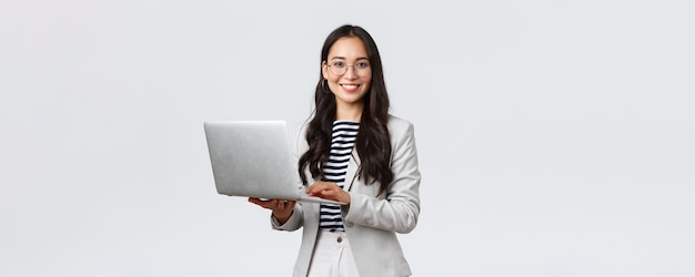 Finanças de negócios e emprego conceito de empreendedores de sucesso feminino Confiante sorridente empresária asiática trabalhadora de escritório em terno branco e óculos usando laptop ajuda clientes