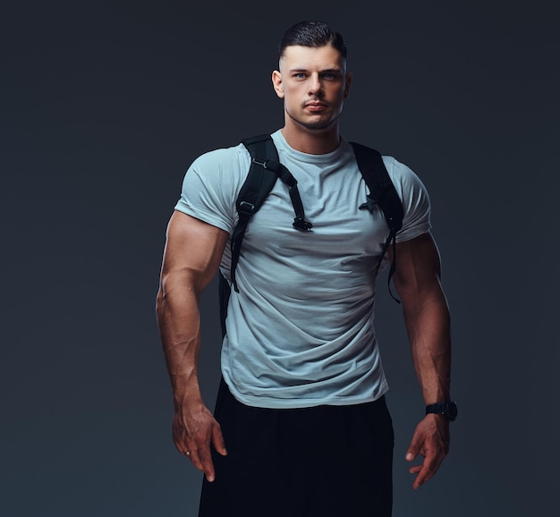 Foto grátis fisiculturista bonito musculoso em roupas esportivas com mochila posando contra um fundo cinza.