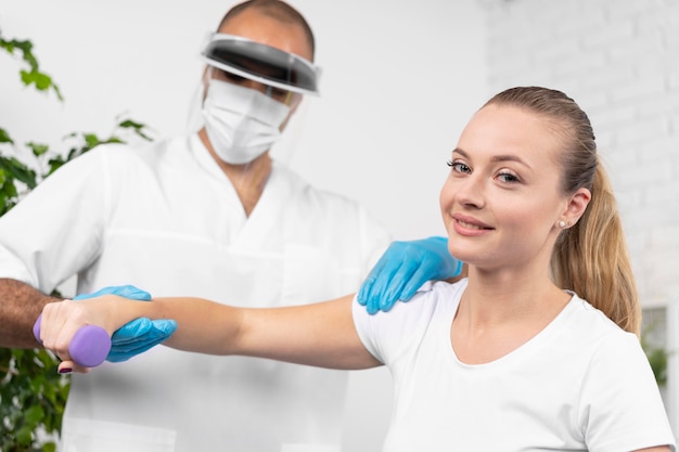 Fisioterapeuta masculino com máscara médica e protetor facial, verificando o braço da mulher