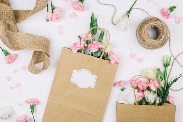 Fita de juta; carretel de linha e papel sacolas com eustoma e cravos flores sobre fundo branco