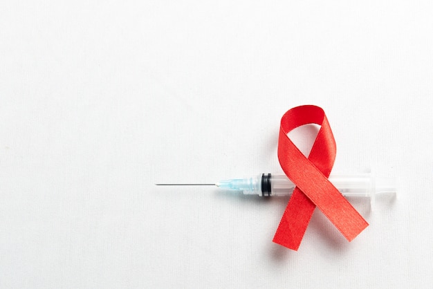 Fita vermelha e seringa com fundo branco. conscientização da fita hiv-aids