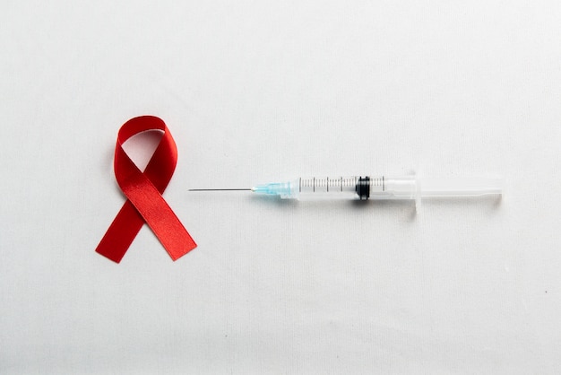 Fita vermelha e seringa com fundo branco. Conscientização da fita HIV-Aids