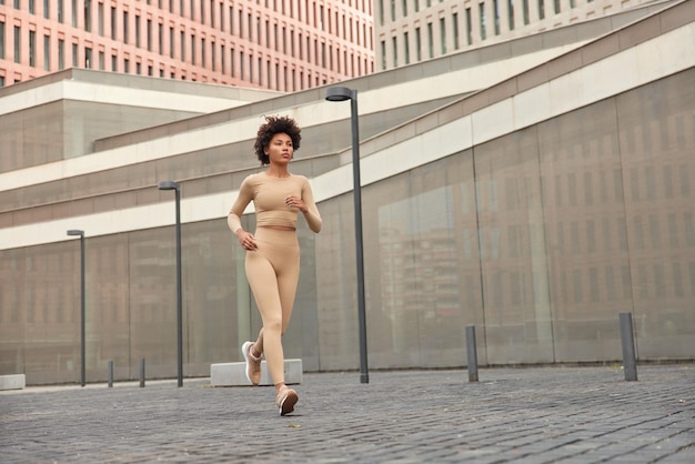 Fitness e conceito de corrida. foto de corpo inteiro de uma corredora ativa vestida com roupas esportivas e tênis correndo durante a manhã em um local urbano