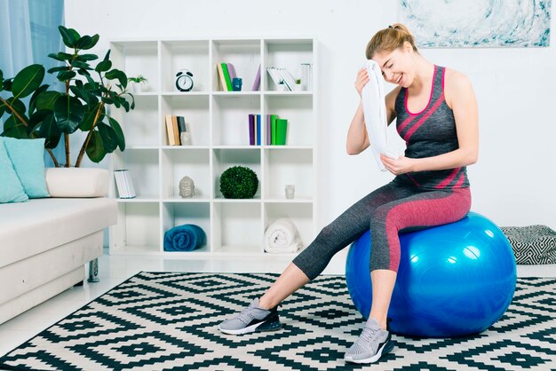 Fitness jovem mulher sentada na bola de pilates azul, limpando o suor com toalha