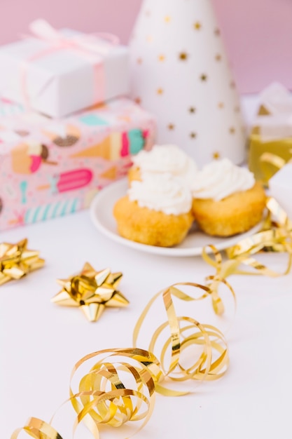 Flâmulas de redemoinho na frente do cupcake de desfoque; presentes e chapéu de festa na mesa branca