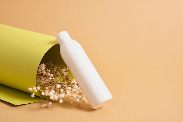 Flor e garrafa para cosméticos, conceito de cosméticos naturais de papel texturizado verde laminado, fundo bege