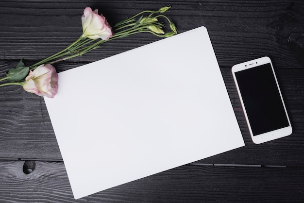 Flor Eustoma com papel branco em branco e telefone celular na mesa de madeira