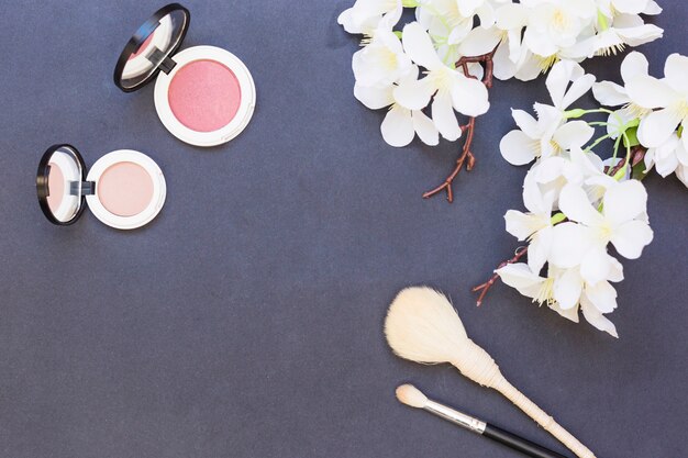 Flores brancas; blush rosa e bege com dois pincel de maquiagem em fundo cinza